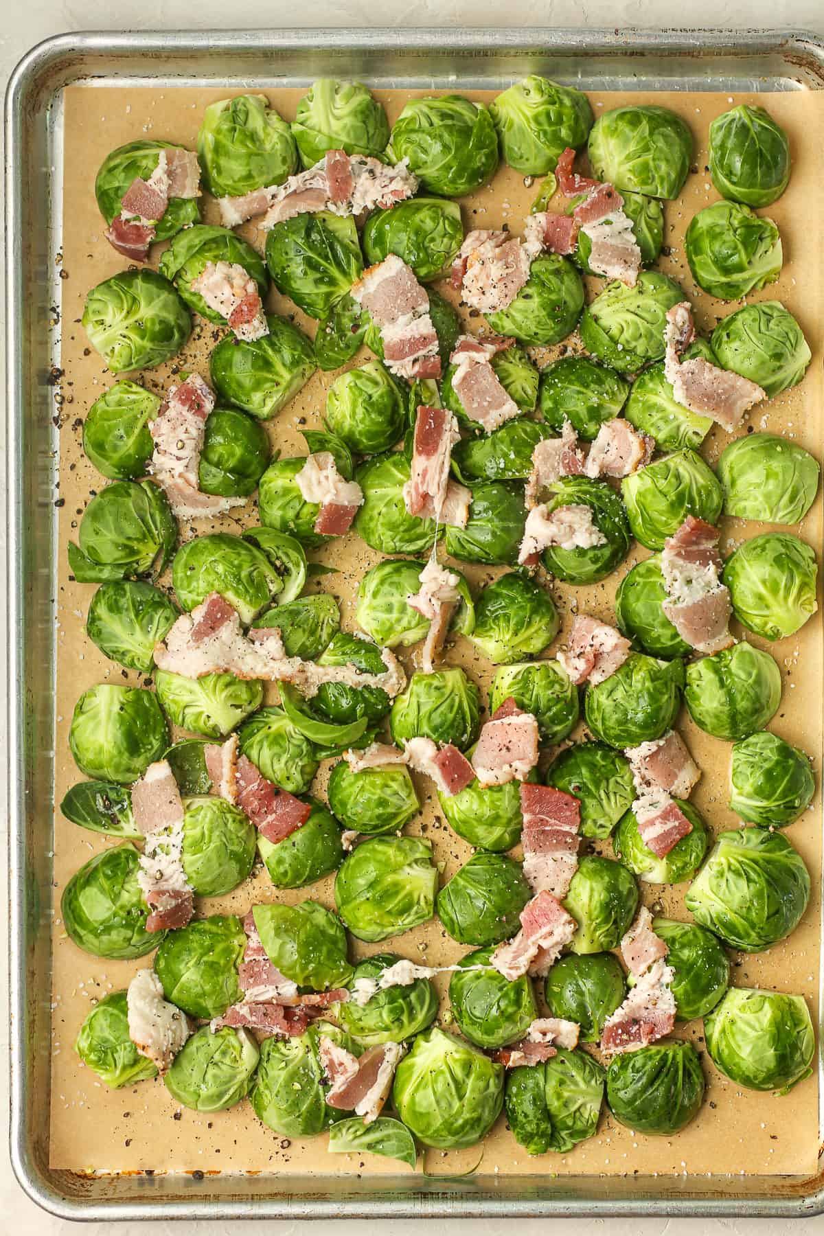 A pan of halved Brussels sprouts and raw bacon before roasting.