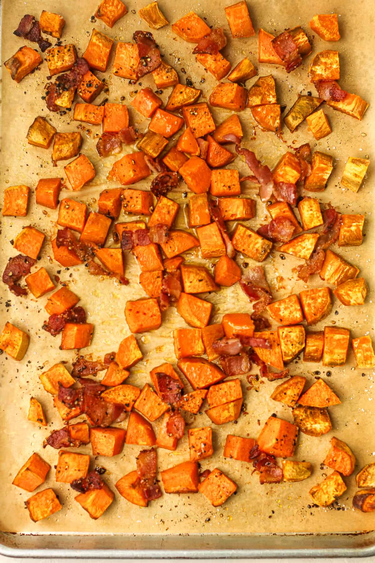 A sheet pan of chopped sweet potatoes with bacon after roasting.