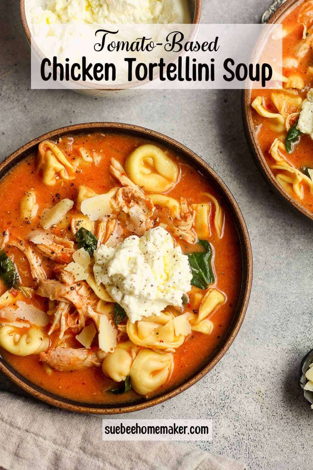 A shallow bowl of tomato-based chicken tortellini soup with ricotta cheese on top.