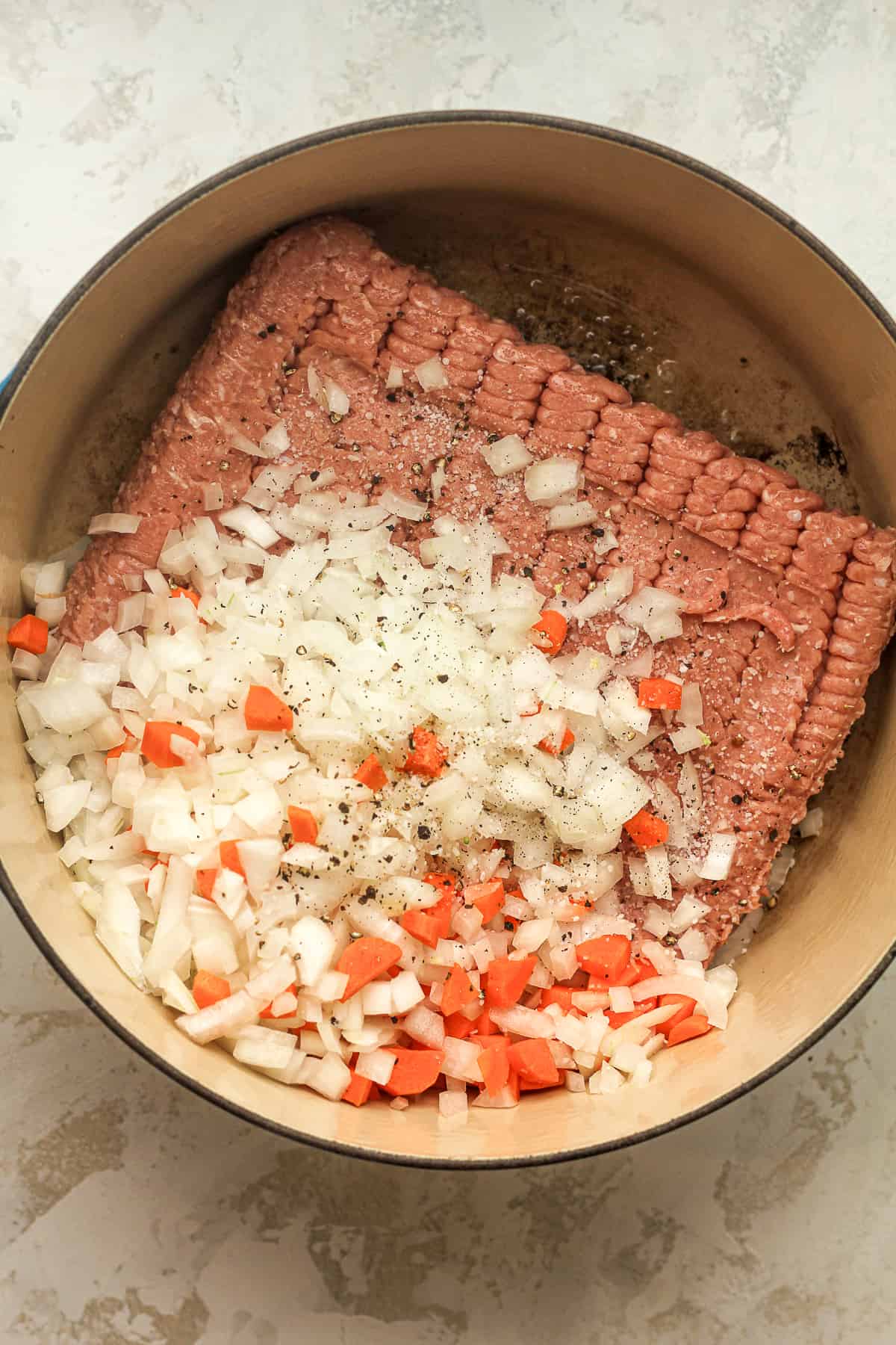 A pot of the raw ground turkey and onions and carrots on top.