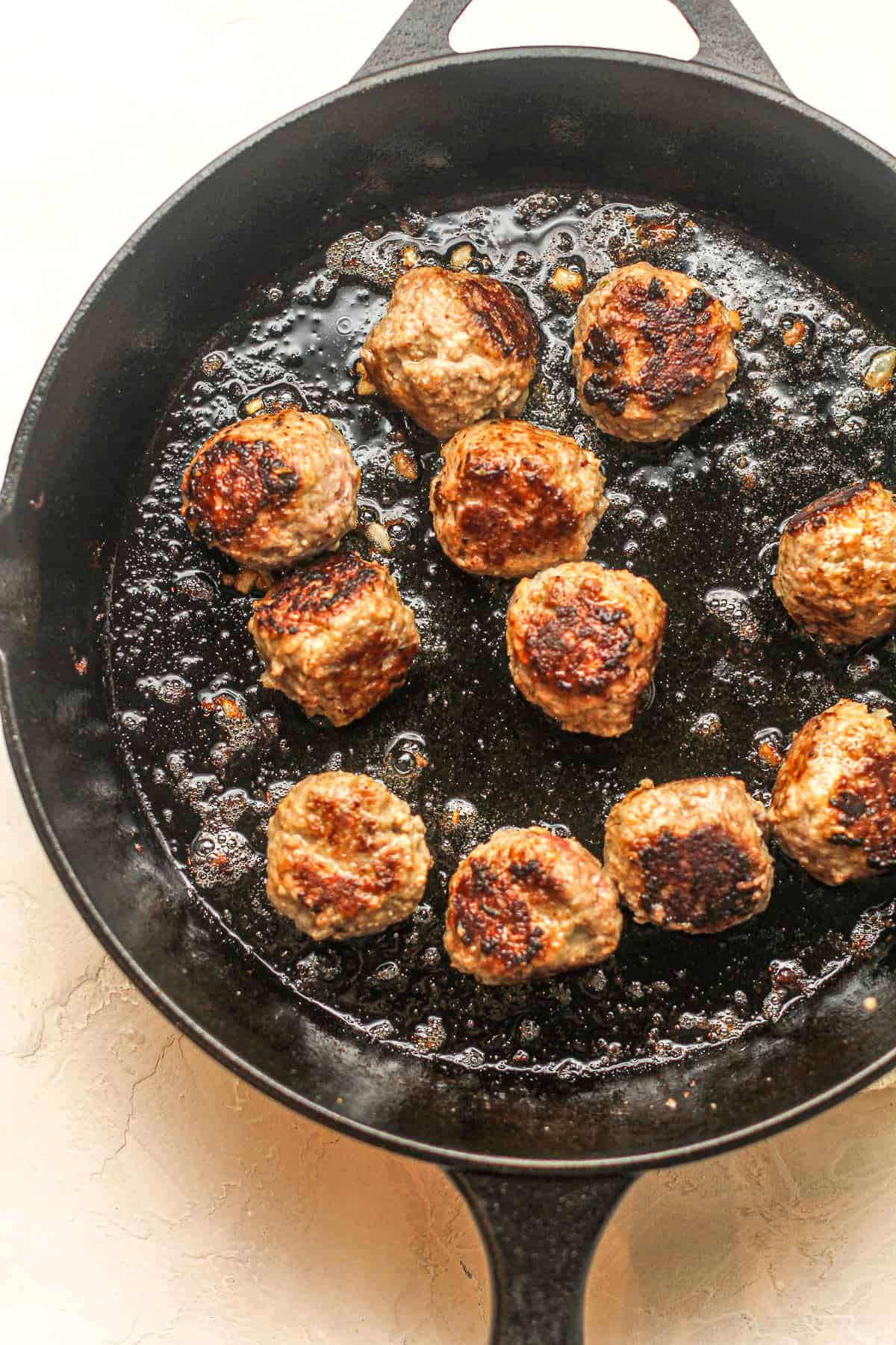 A cast iron skillet of cooked meatballs.