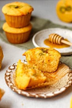 Side view of a small plate of a halved cornbread muffin with honey.