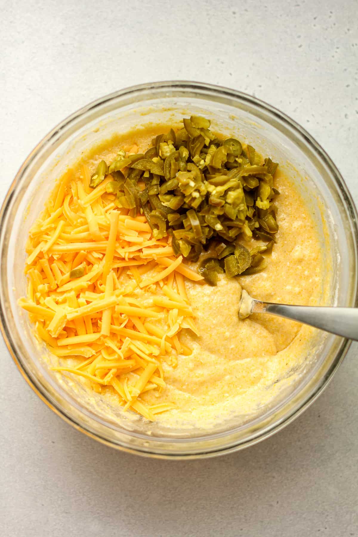 A bowl of the cornbread batter with chopped jalapeños and shredded cheddar cheese.