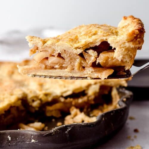 A caramelized apple pie with a slice lifted over the top.