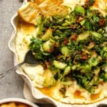 Closeup on a pie plate of warm goat cheese dip with brussels sprouts on top - plus crackers.