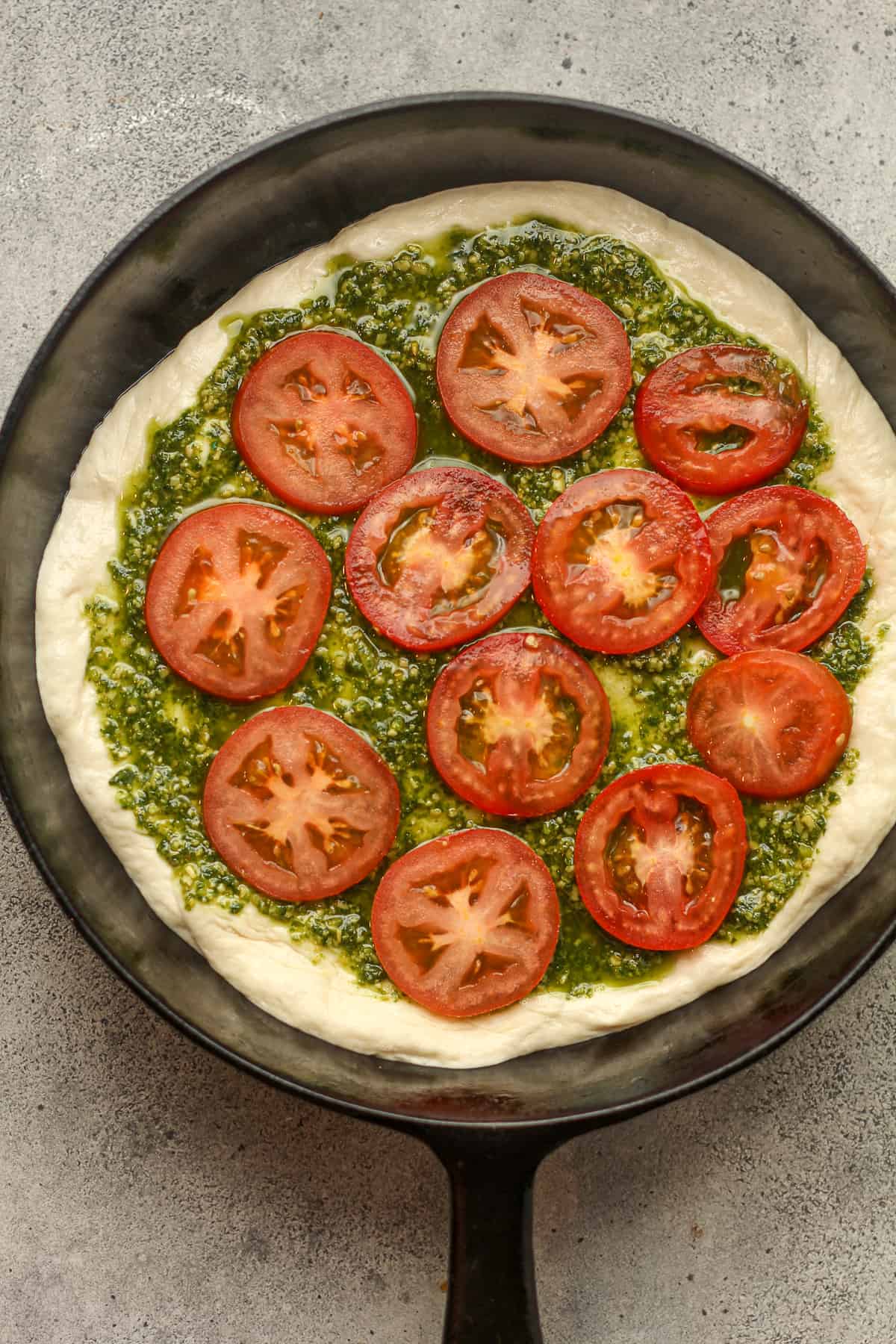 A skillet of the dough with pesto sauce and sliced tomatoes.