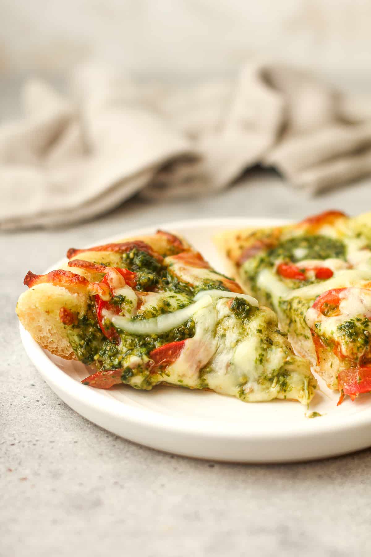Side view of a plate with two slices of pesto pizza.