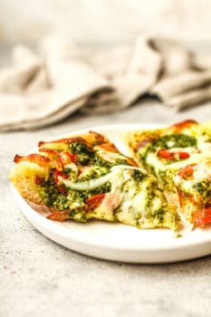 Side view of two slices of pesto pizza on a plate.