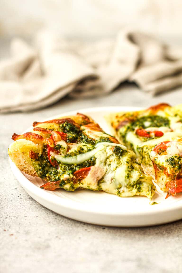 Side view of two slices of pesto pizza on a plate.