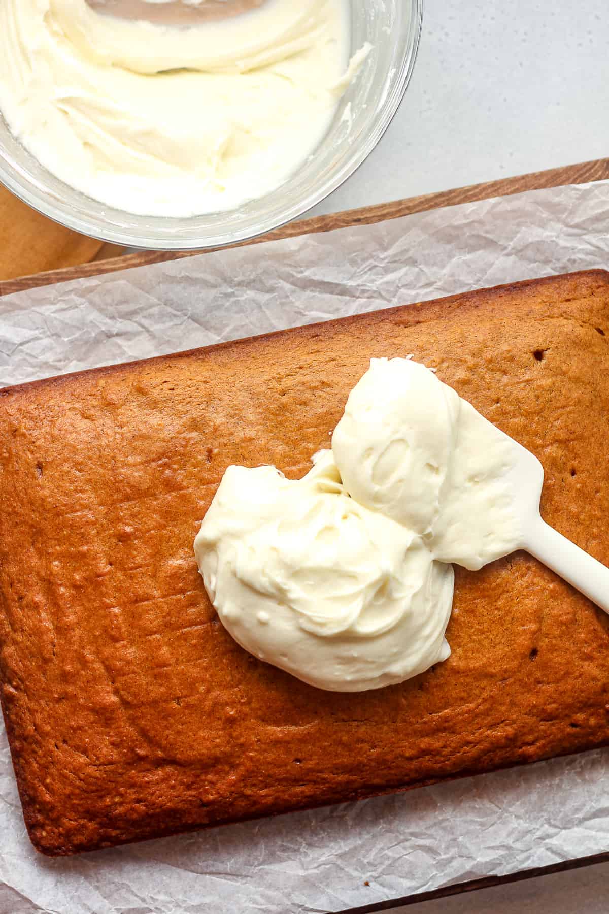 A pumpkin cake with some frosting plopped on top with a spatula.