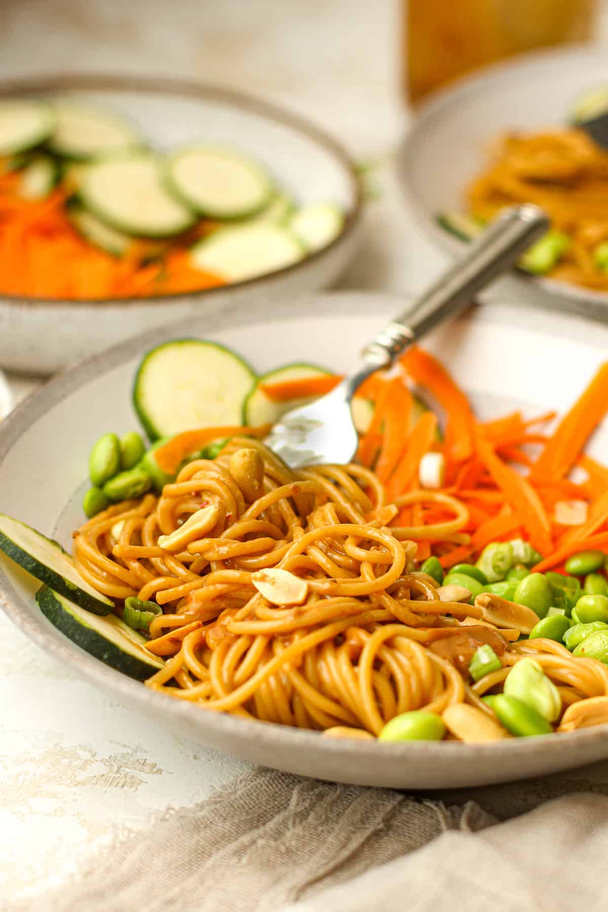 Side view of two bowls of spicy peanut noodles with veggies.