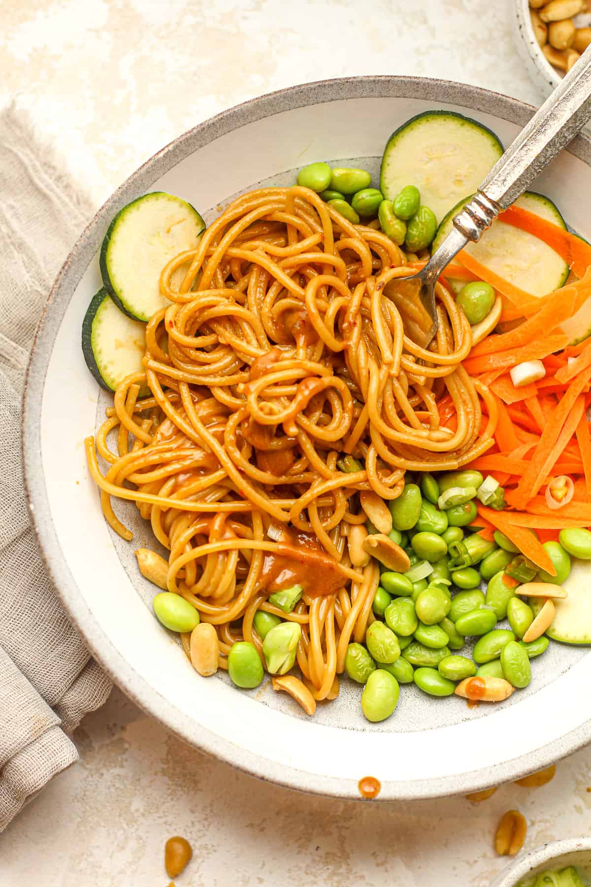 Closeup on a bowl of spicy peanut noodles with zucchini and carrots.