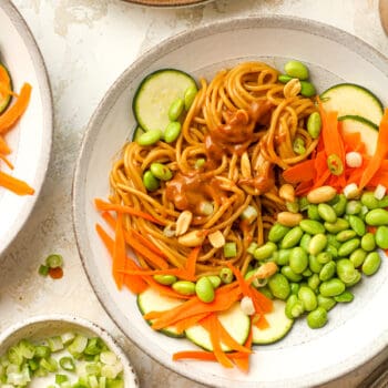 Closeup shot of a bowl of spicy peanut noodles with zucchini, carrots, and edamame.