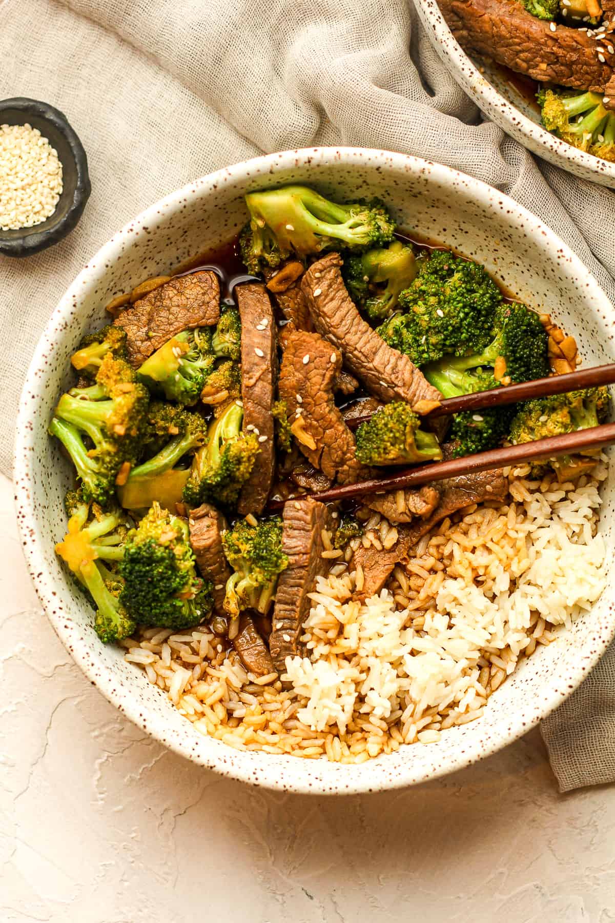 Two bowls of beef and broccoli stir fry with sesame seeds.