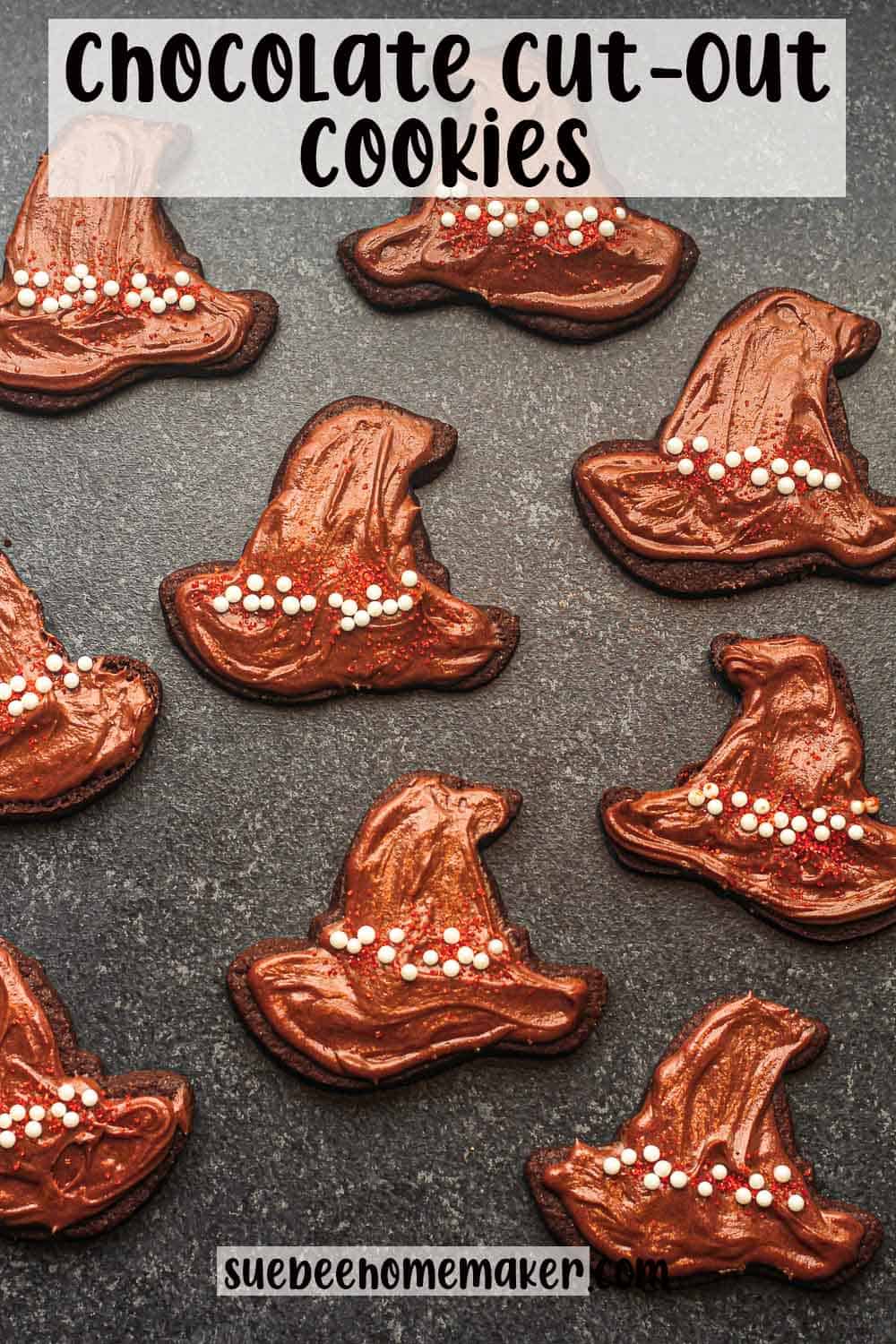 Some frosted chocolate cut out witch hats on a black surface.