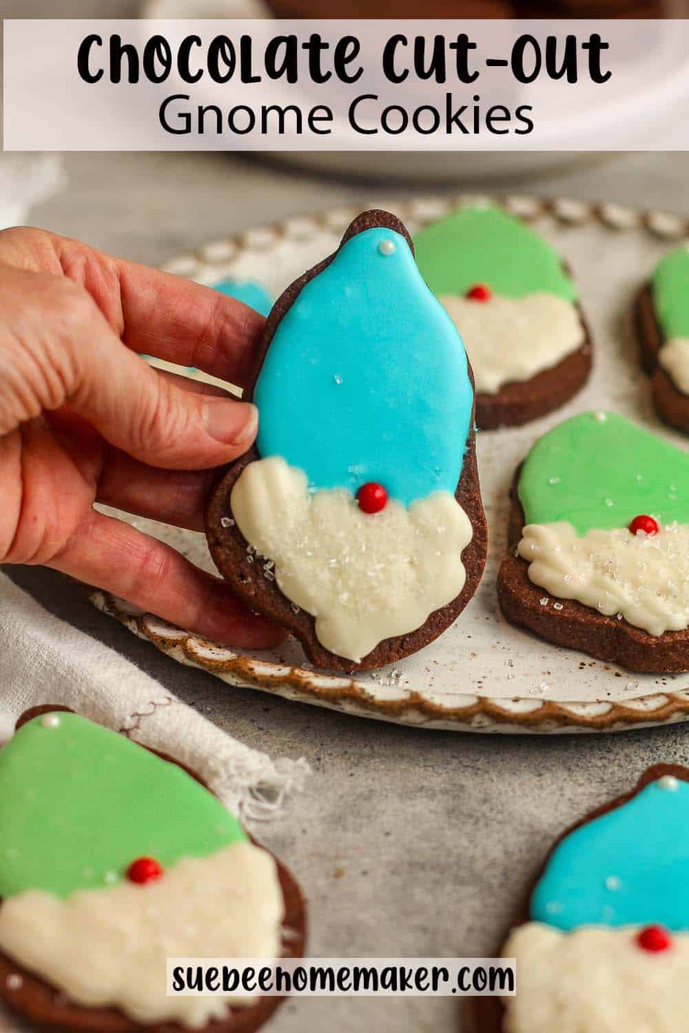A hand holding a chocolate cut-out gnome cookies over a plate of cookies.