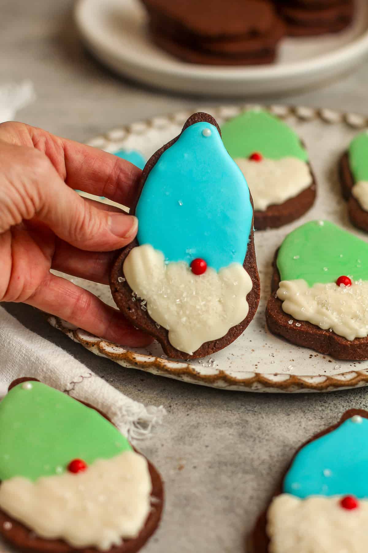 Side view of a pate of cookies with my hand holding one gnome cookie with a blue hat.