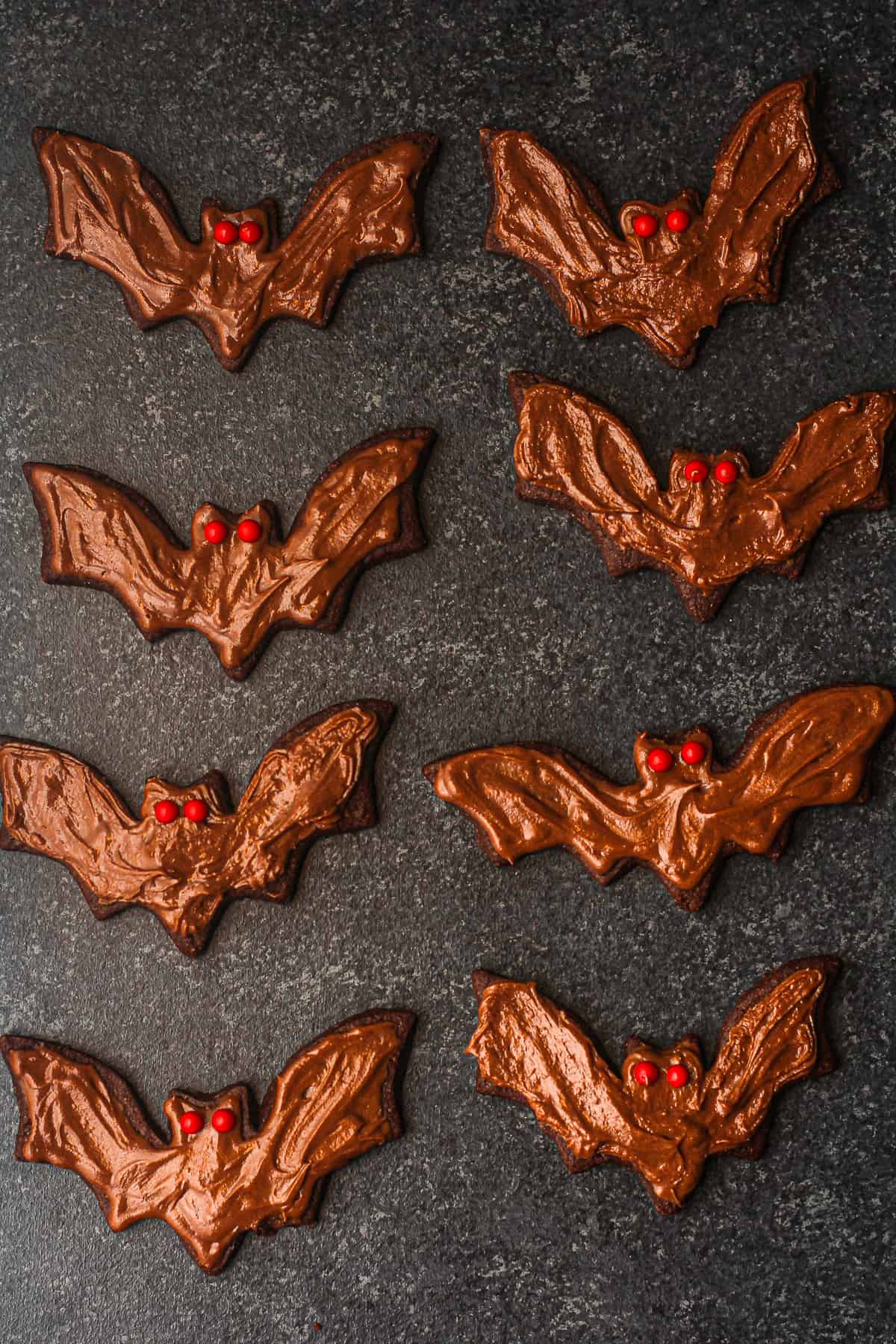 Overhead view of several decorated bat cut-out cookies with red eyes.