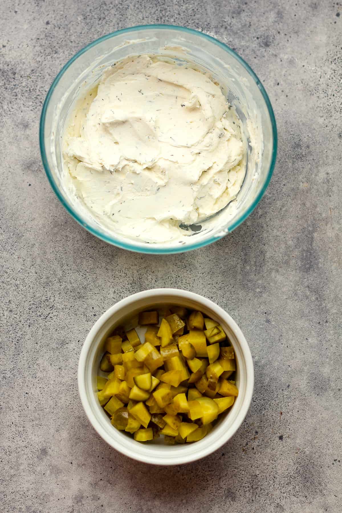 A bowl of the cream cheese mixture and a bowl of the diced dill pickles.