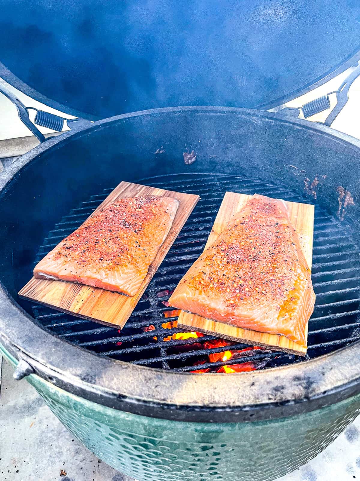Two pieces of raw salmon on cedar planks on a grill.