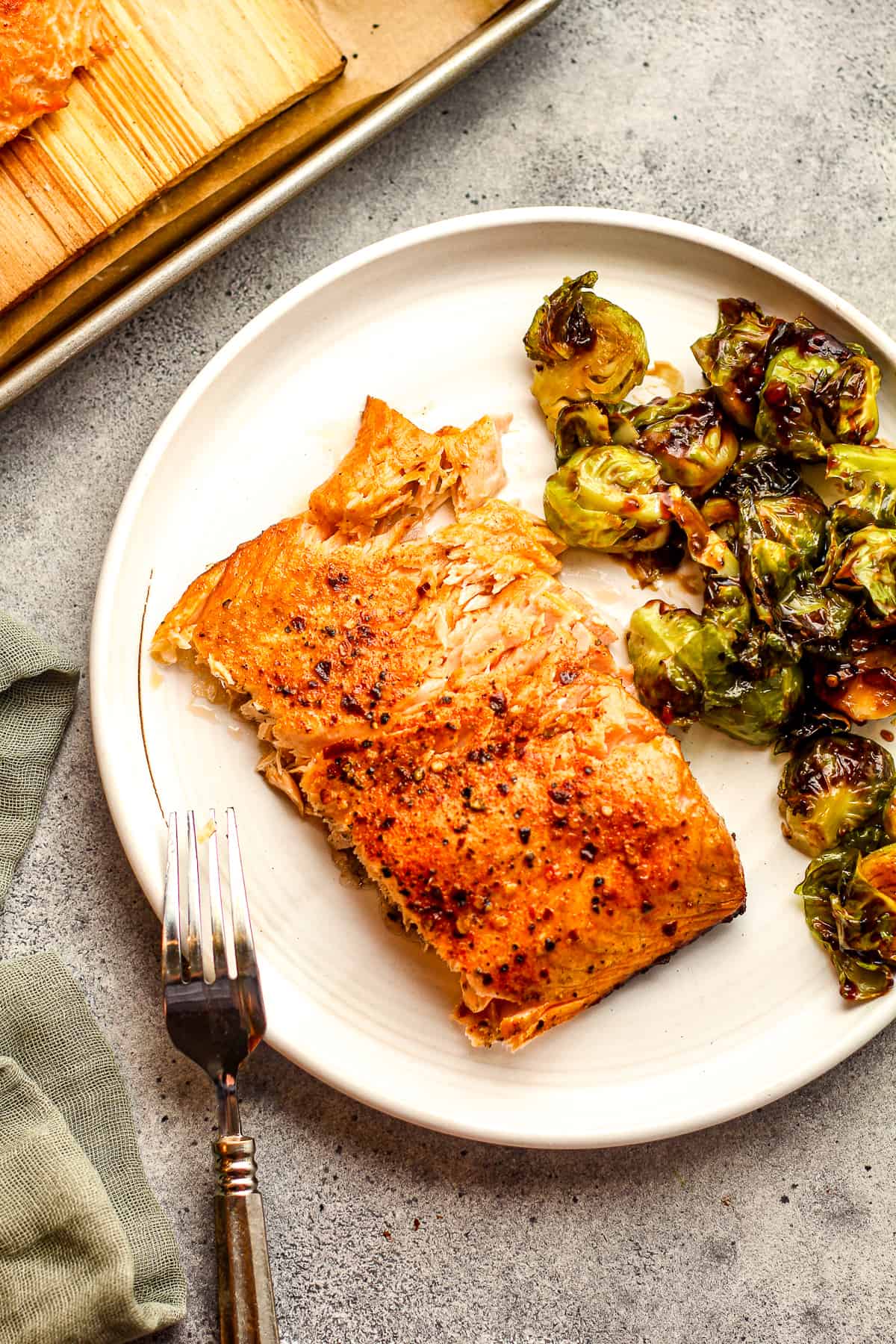 A plate with a large piece of cedar plank salmon plus teriyaki brussels sprouts.