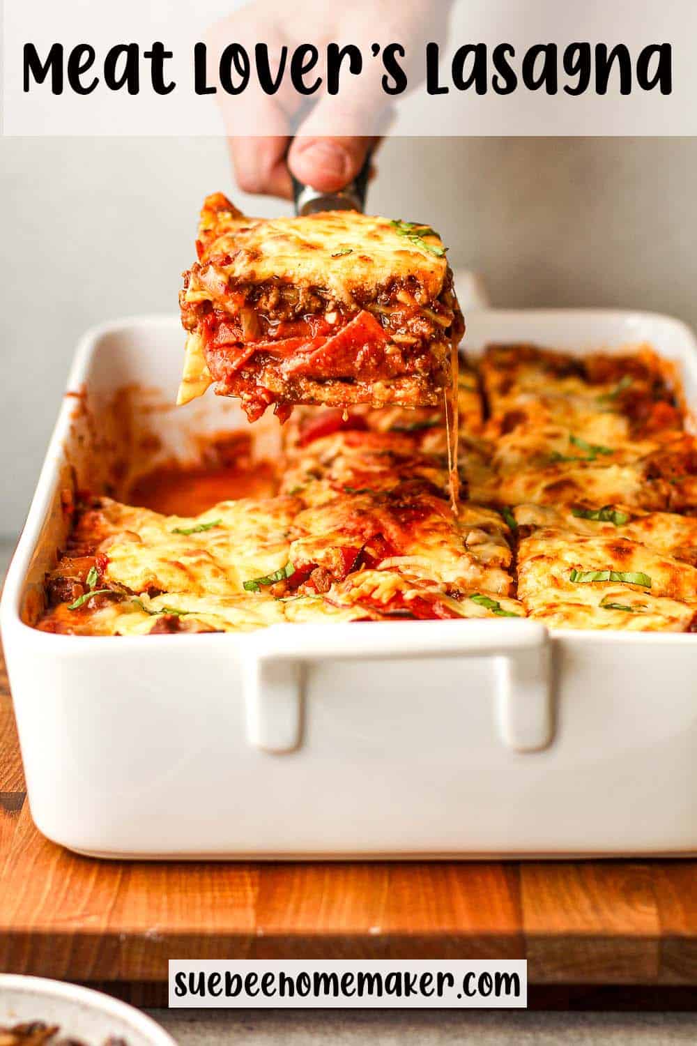 A hand using a spatula to hold up a large piece of meat lover's lasagna.