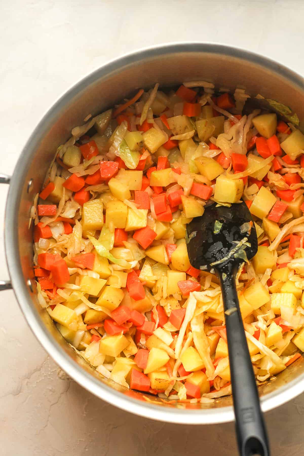 A large pot of sautéed onions, carrots, cabbage, and potatoes.