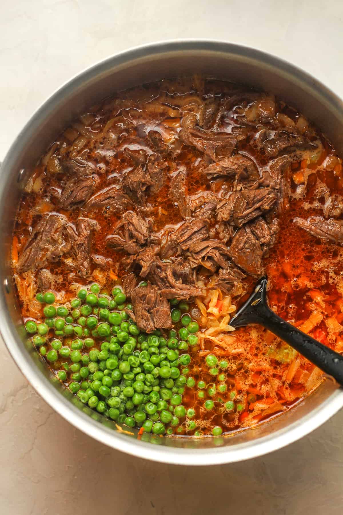 A large pot of soup with shredded beef and peas on top.