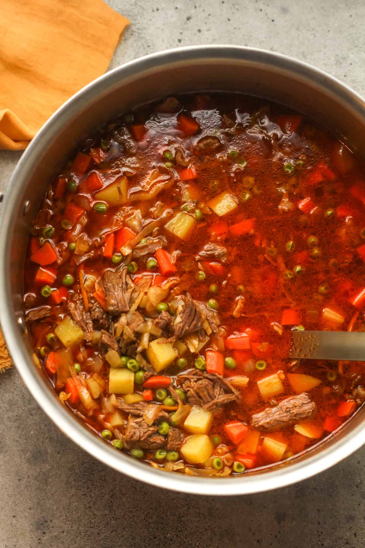 A large pot of roast beef soup with a soup ladle inside.