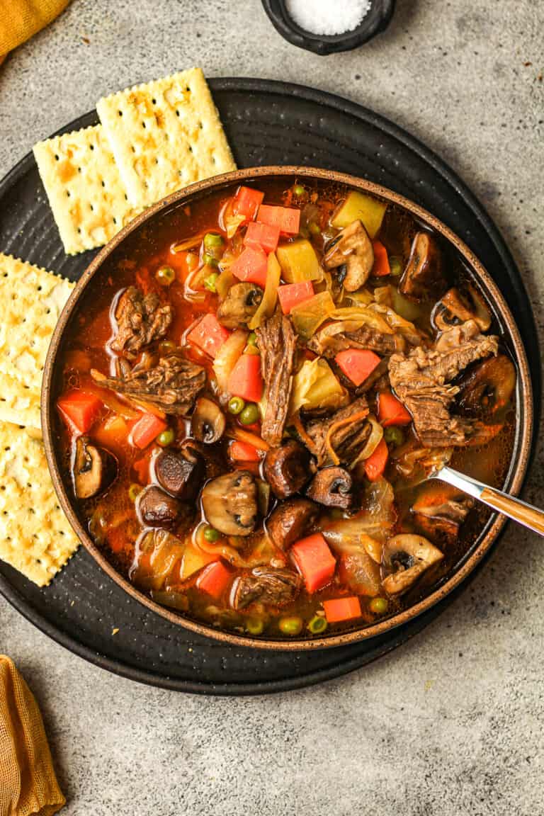 Overhead shot of a bowl of beef vegetable soup with some saltine crackers.