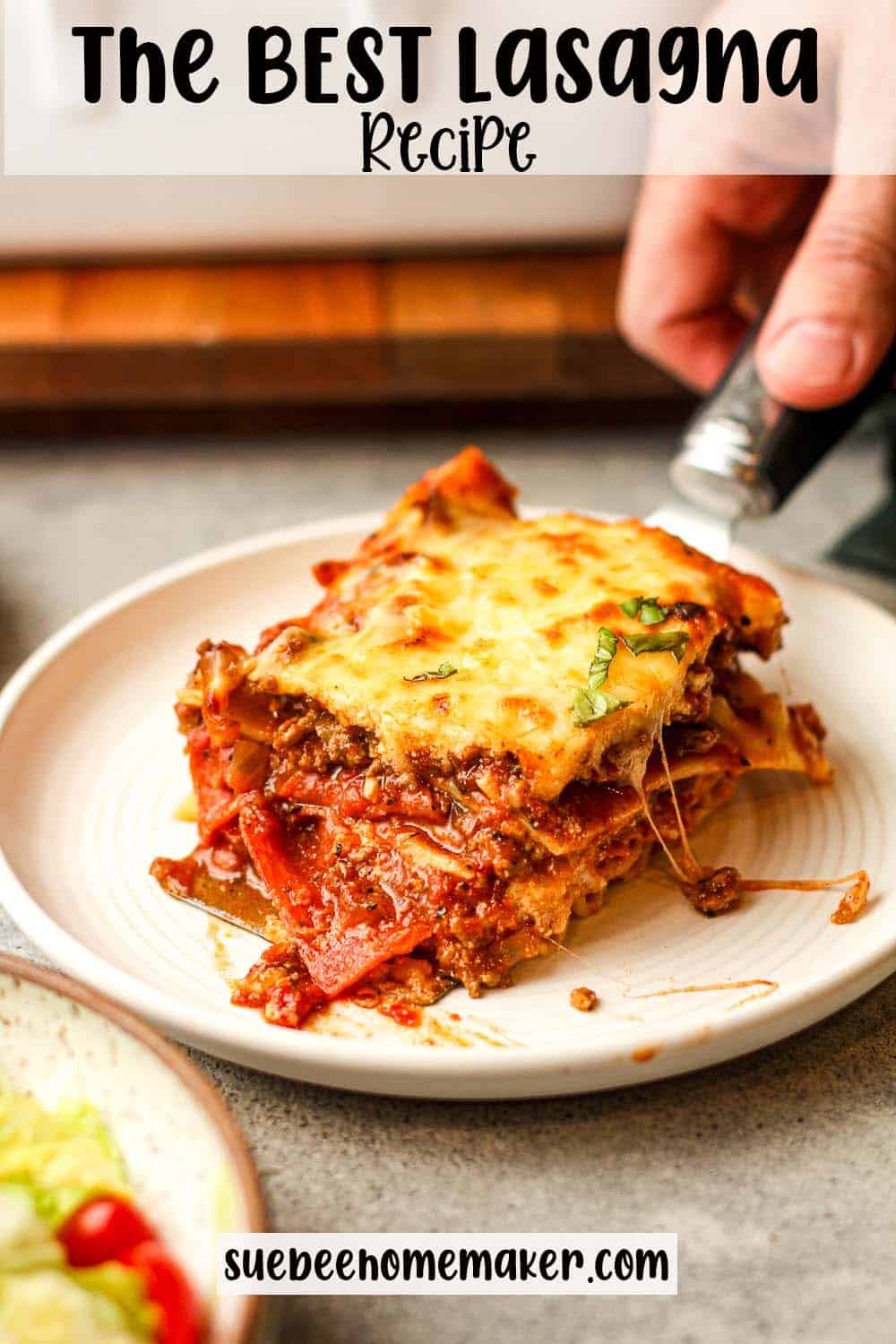 Side view of a hand placing a piece of lasagna on a serving plate.