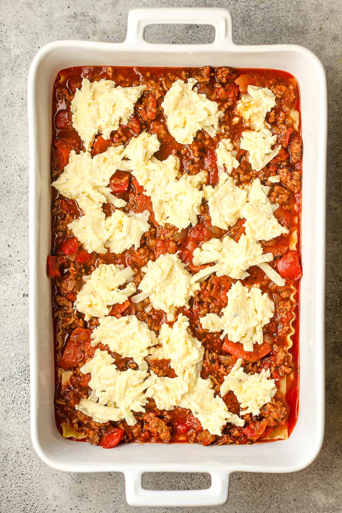 A casserole dish of the lasagna with the ricotta cheese mixture on top.