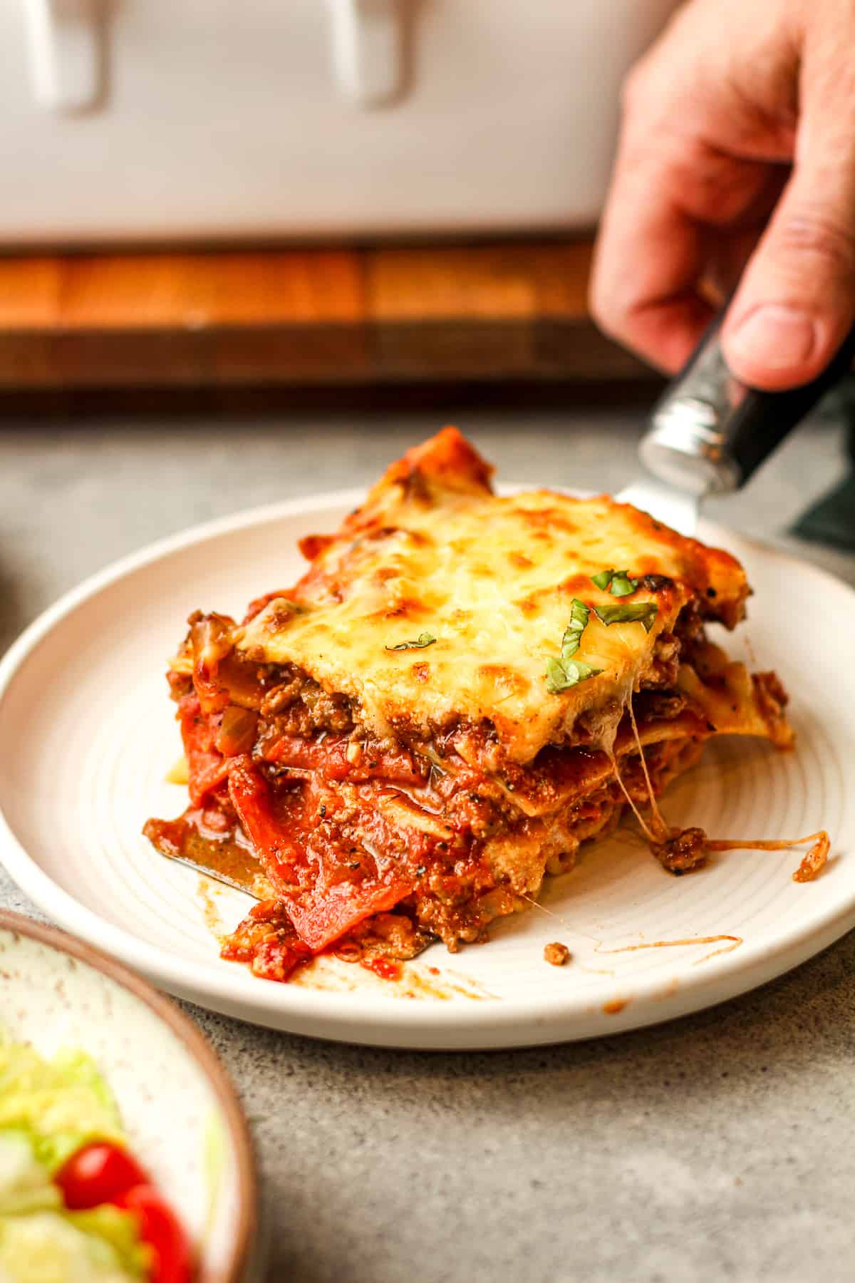 A hand serving up a piece of lasagna on a plate.