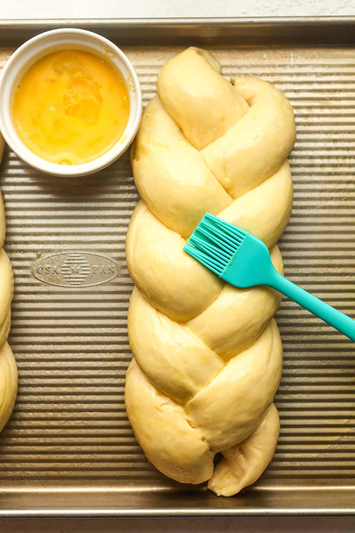 A pan with some braided brioche dough with an egg wash.