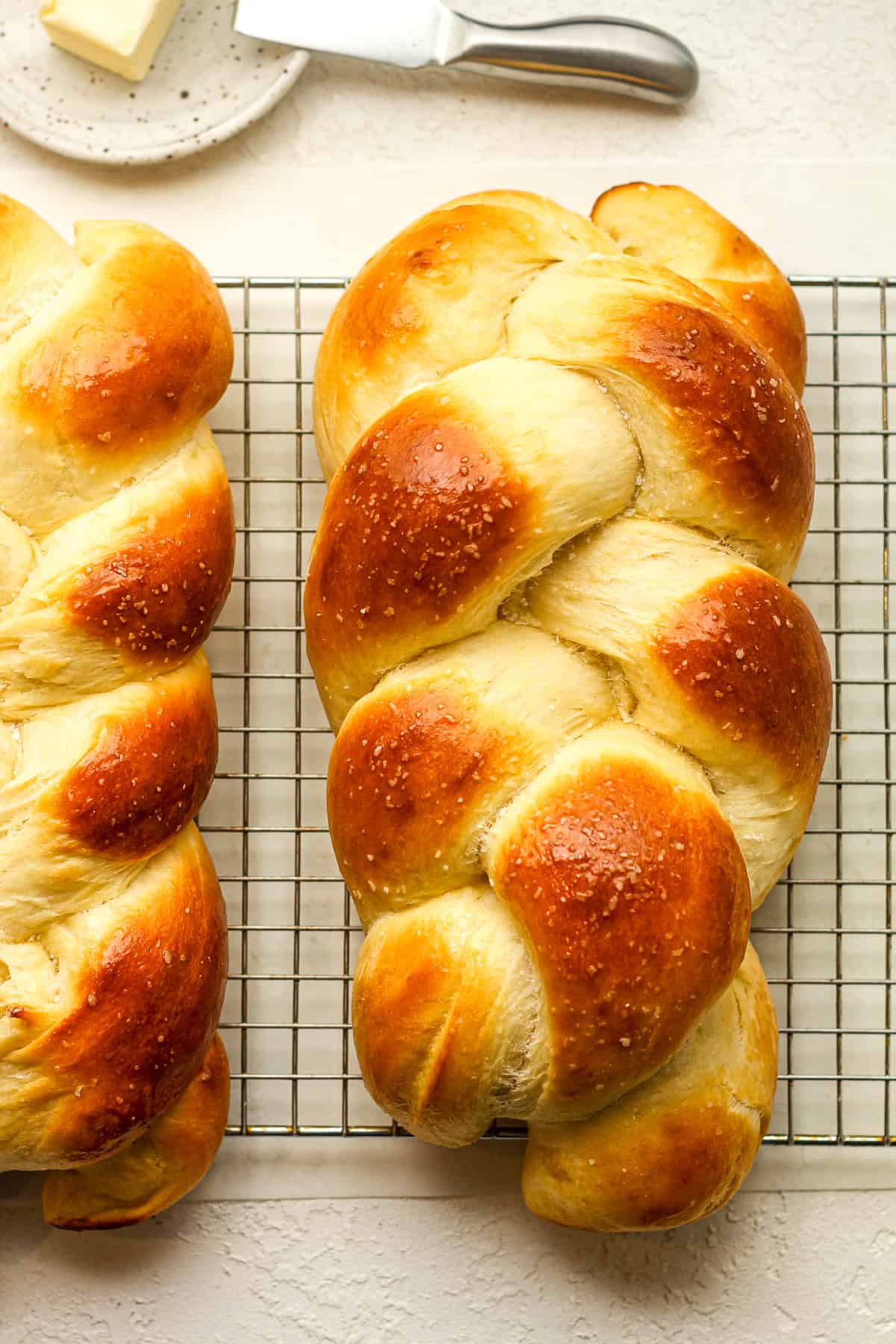 Two loaves of braided brioche bread on a wire rack.
