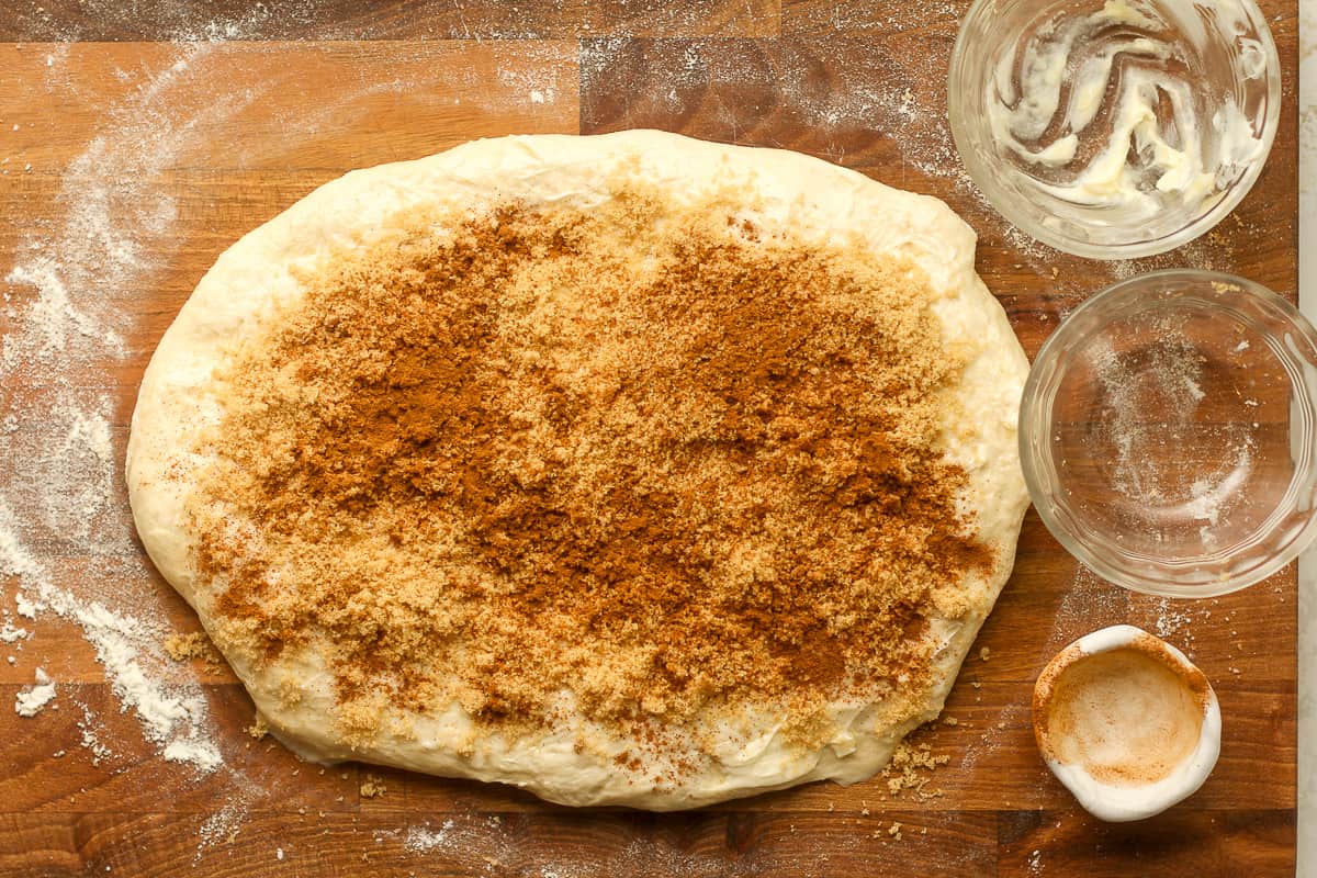 The bread dough on a board flattened out with brown sugar and cinnamon on top.