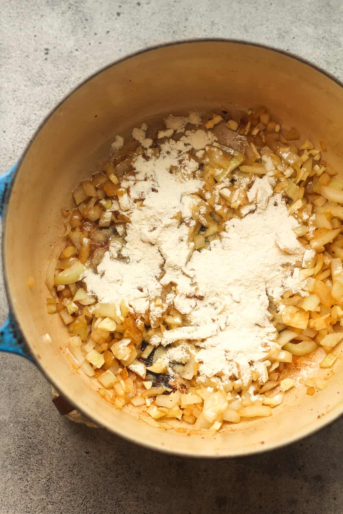 A pot of the sautéed onions and garlic, topped with flour.