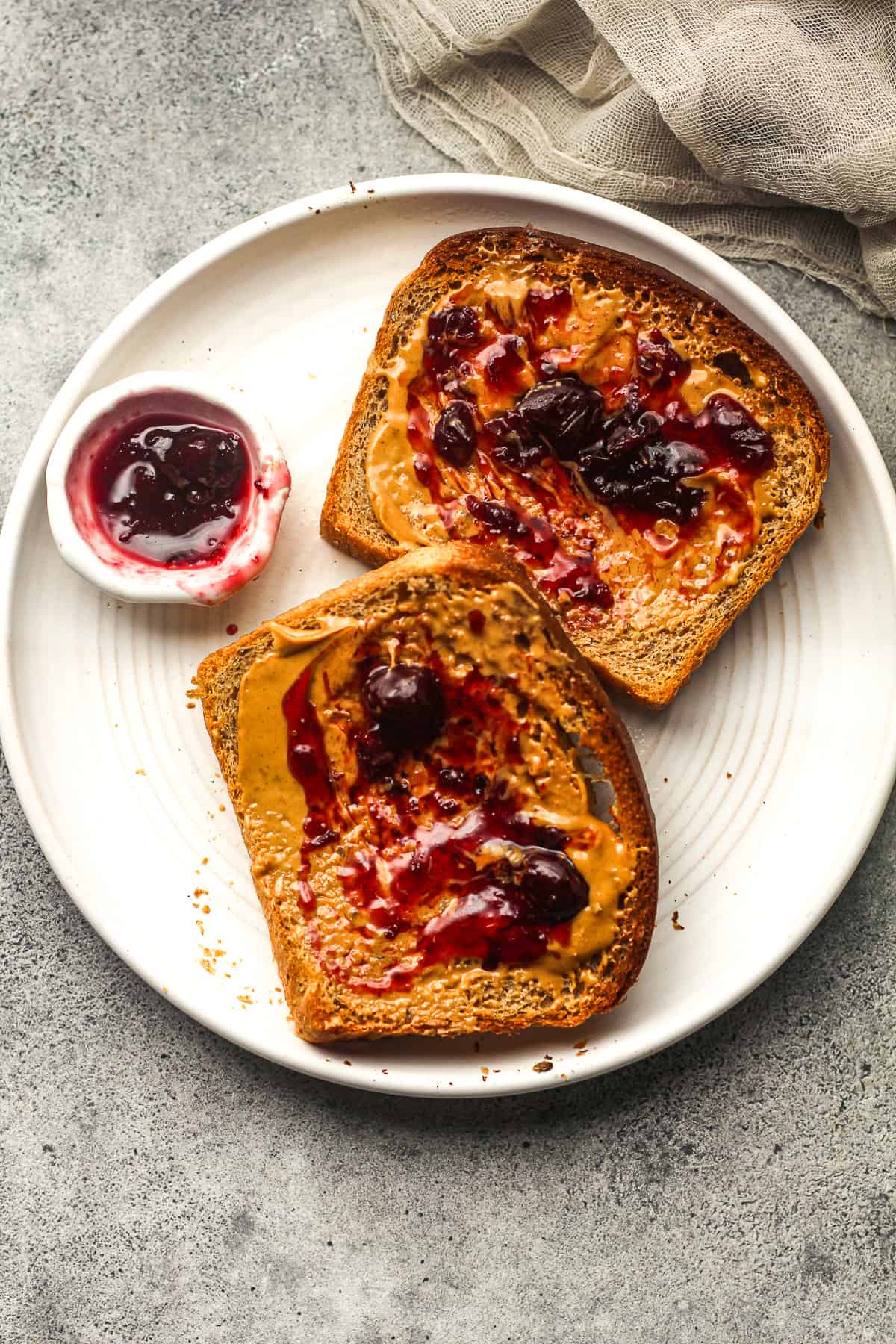 A plate of two pieces of toast with peanut butter and jelly.