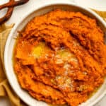 A bowl of mashed sweet potatoes with butter on top.