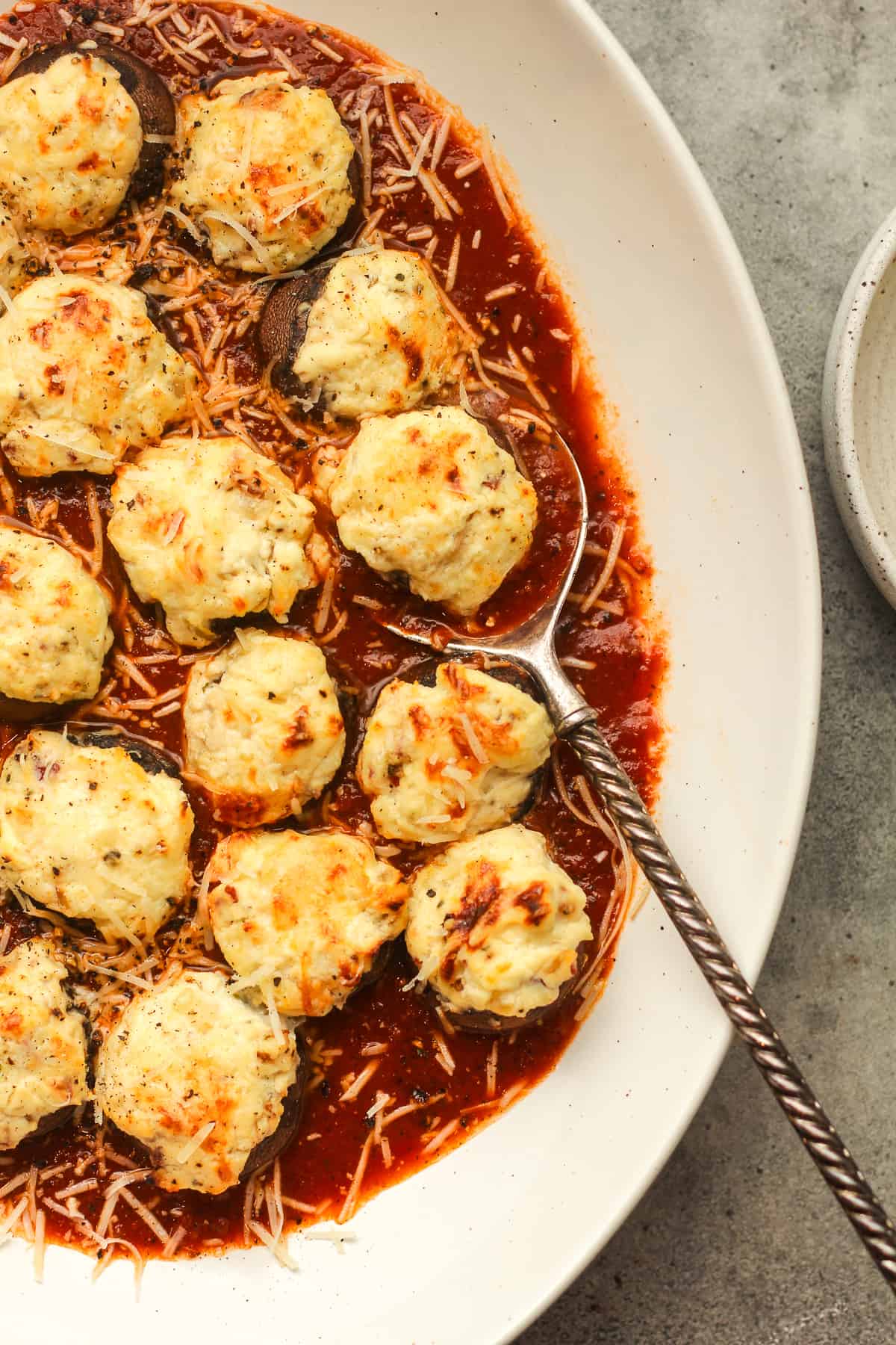 Overhead view of a platter of ricotta stuffed mushrooms over red sauce with a spoon.