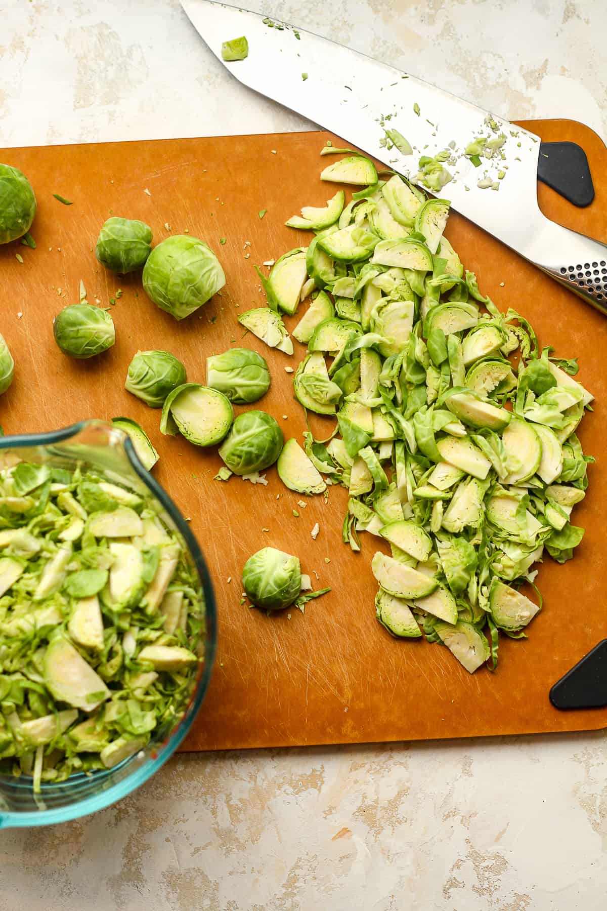 A cutting board with a knife after thinly slicing Brussels sprouts.