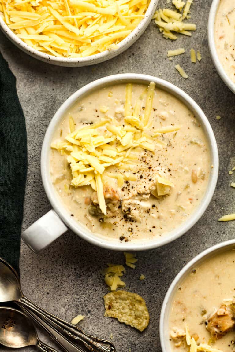 Overhead view of a mug of chicken chili with shredded white cheese.