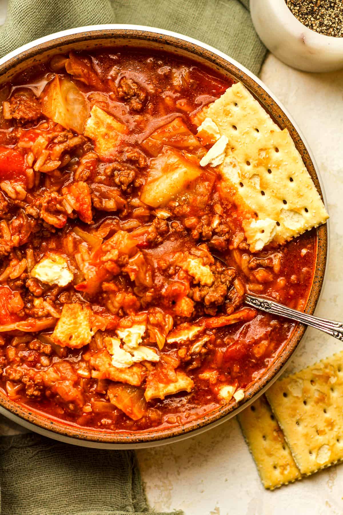 A bowl of cabbage soup with ground beef and crackers.