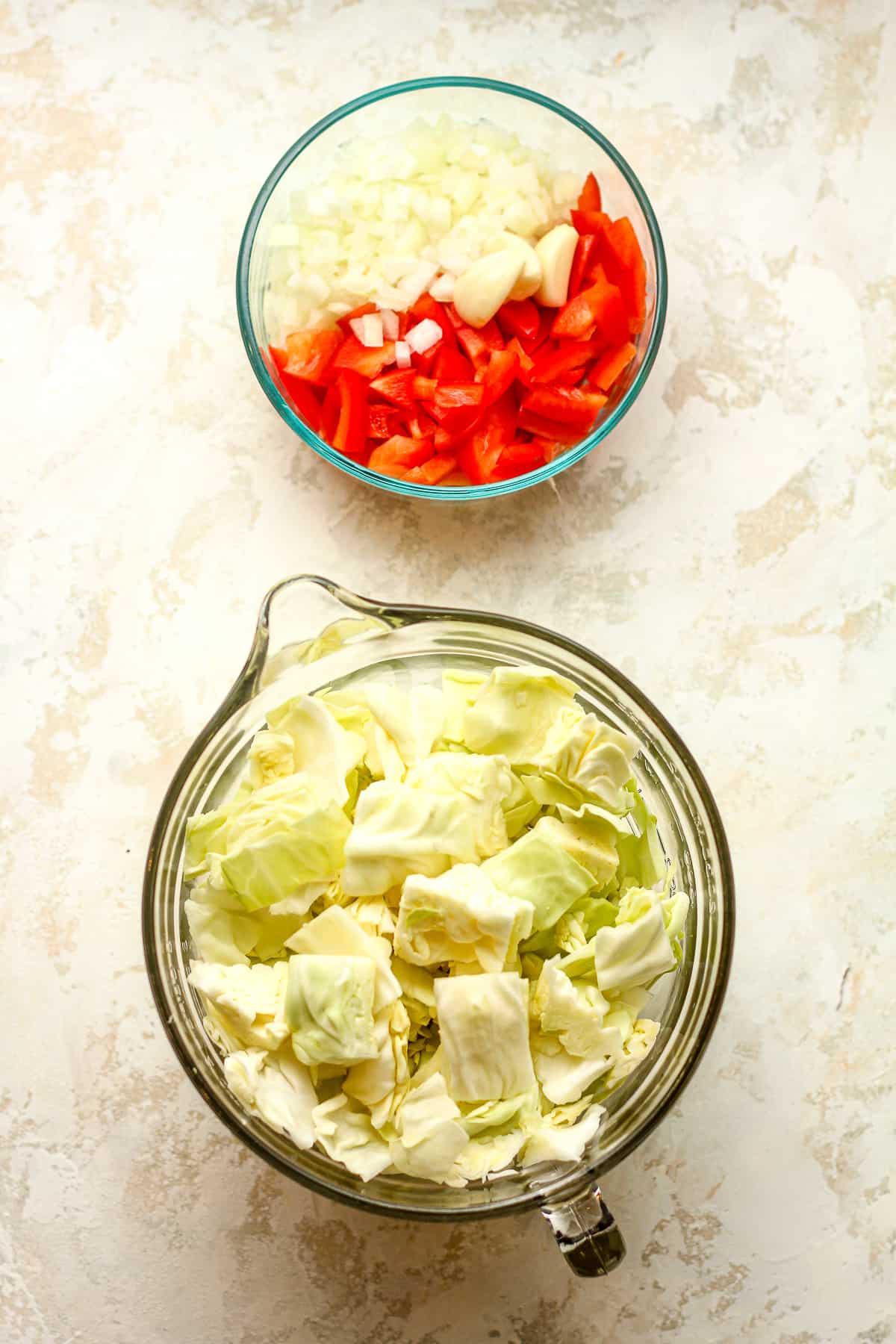 A bowl of the diced onion and peppers and a large measuring cup of the chopped cabbage.