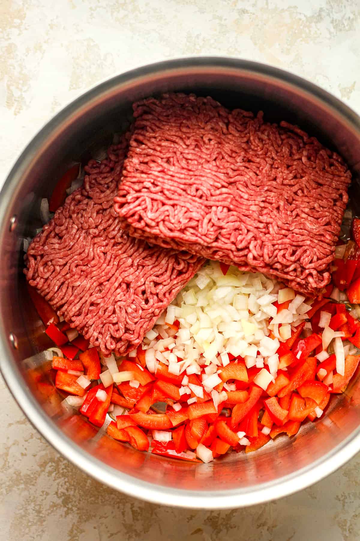 A pot of the onions, bell peppers, and raw ground beef.