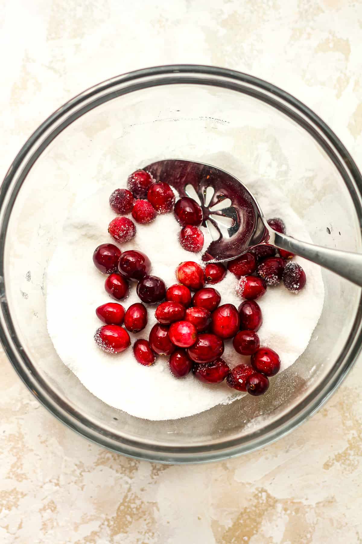 A bowl of sugar with some sticky cranberries on top.