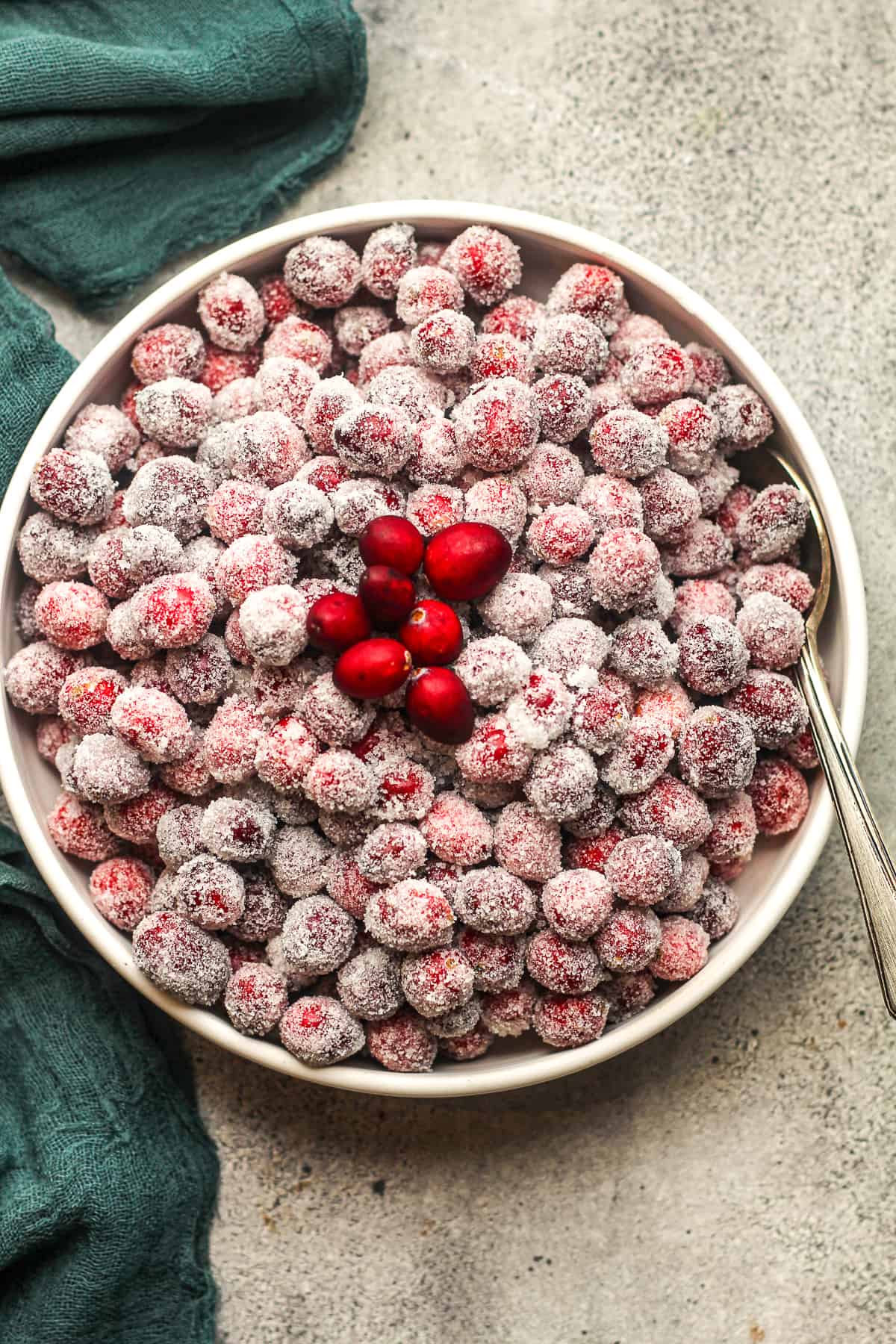 Overhead view of a bowl of sugared cranberries with a green napkin.