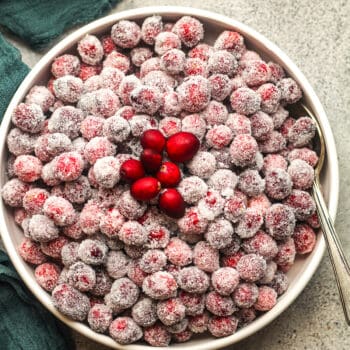 A white bowl of sugared cranberries with a green napkin.