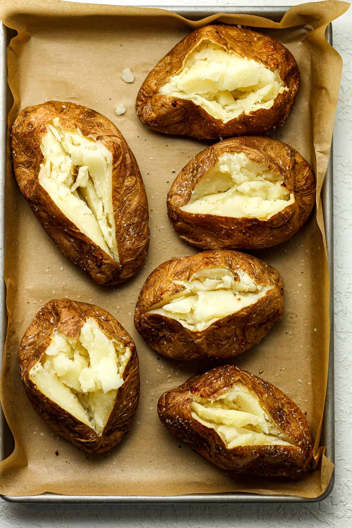 Six baked potatoes on a sheet pan.
