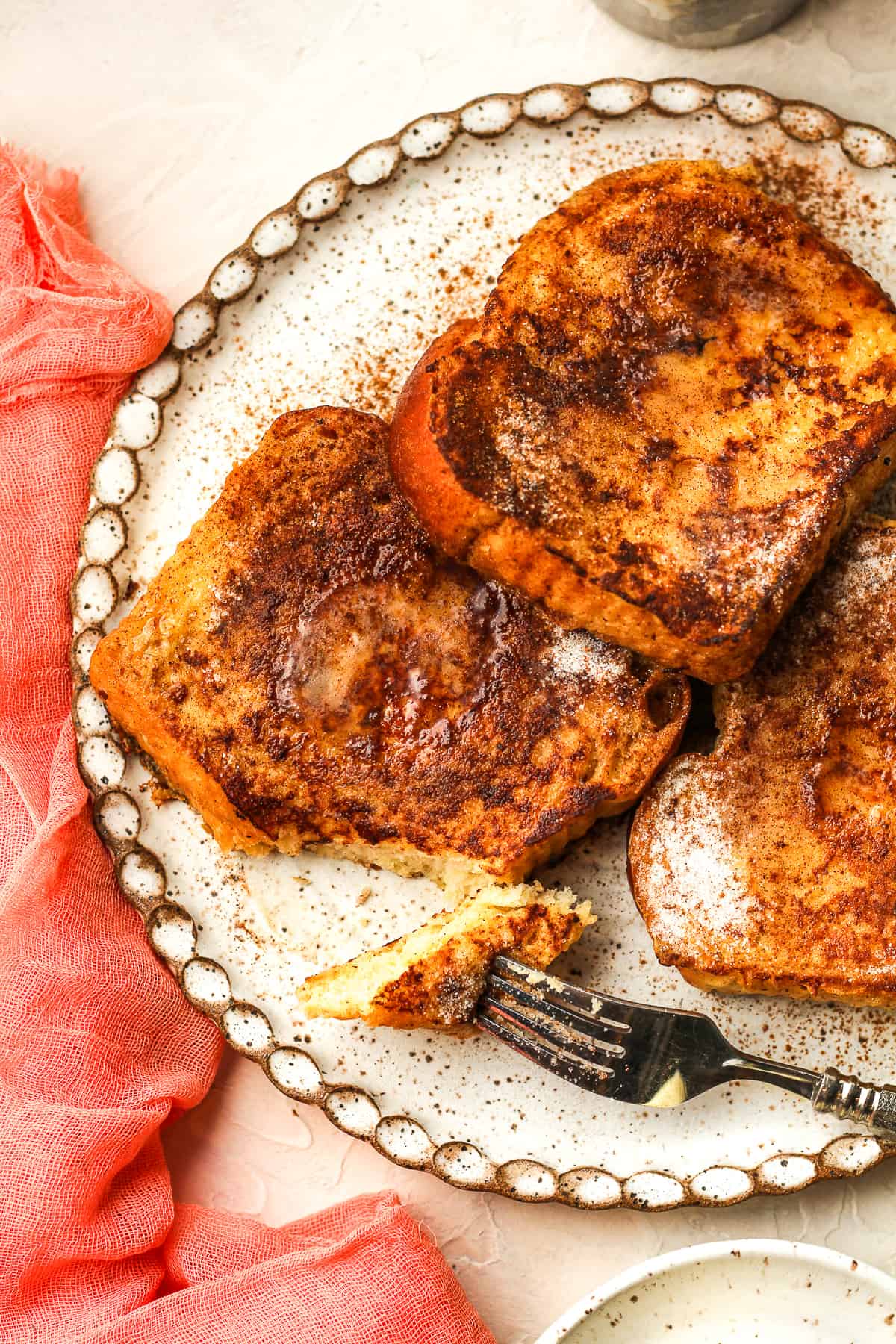 A plate of three pieces of brioche French toast with a fork.